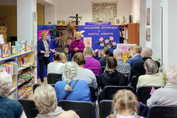 Mieszkańcy i uczestnicy spotkania słuchaja wiersza mówionego przez poetkę.