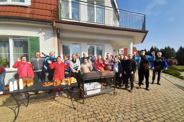 Zdjęcie grupowe mieszkańców machających dłonia przy grillu.