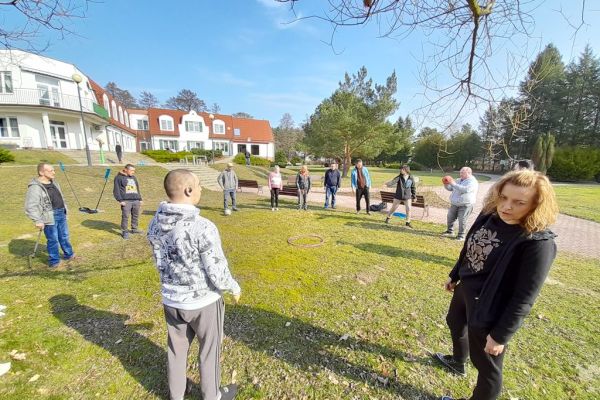 Mieszkańcy ustawieni w duże koło rzucają piłką.