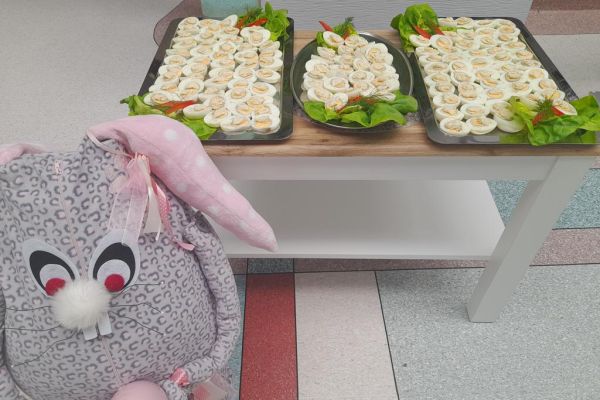 Ułożone jajka na trzech tacach i stojący duży zając.