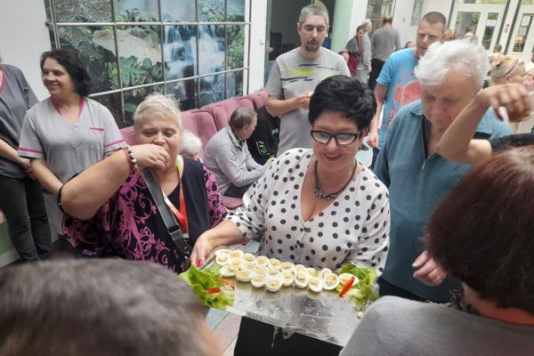 Pani Dyrektor częstuje jajkiem mieszkańców wokół siebie.