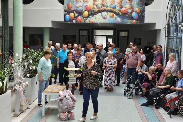 Zgromadzeni mieszkańcy i pracownicy na holu domu podczas częstowania jajkiem przez panią Dyrektor, księgową i Panią Kierownik.