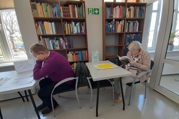 Mieszkańcy czytają przy stolikach w czytelni.