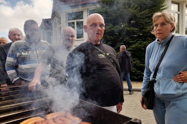 Mieszkańcy czekaja na wysmażenie kiełbaski z grilla.