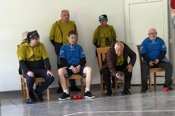 Mieszkaniec wraz z innymi uczestnikami siedzi na krześle i rzuca w cel.