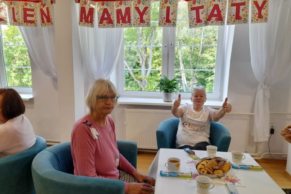 Mieszkańcy siedzą przy stolikach z poczęstunkiem w kawiarence.