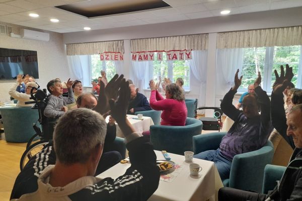 Mieszkańcy siedzą przy stolikach z poczęstunkiem w kawiarence.