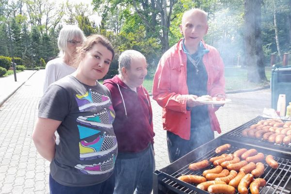 Mieszkańcy stoją przy grillu z kiełbaską.