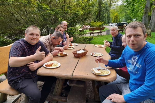 Mieszkańcy jedzą kiełbaskę przy ogrodowym stole.