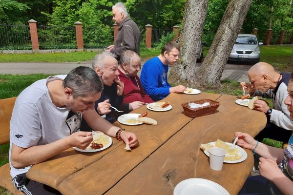 Mieszkańcy jedzą kiełbaskę przy ogrodowym stole.