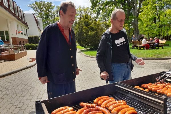Mieszkańcy stoją przy grillu z kiełbasa.
