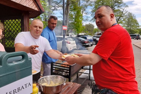 Mieszkaniec odbiera od kucharza talerzyk z kiełbasą.