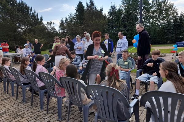 Uczestnicy pikniku siedzą na plastykowych krzesłach podczas zabawy.