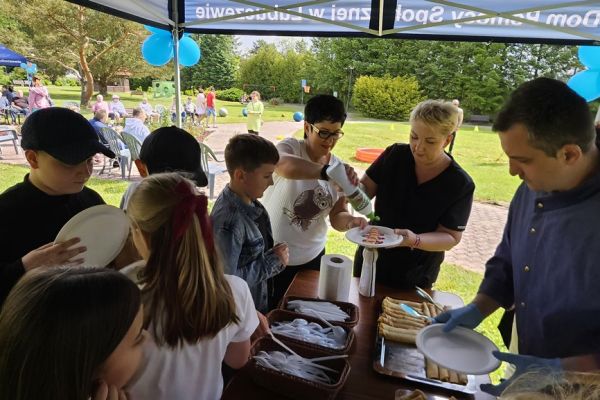Uczestnicy pikniku pobieraja poczęstunek na talerzykach na powietrzu od kucharza.