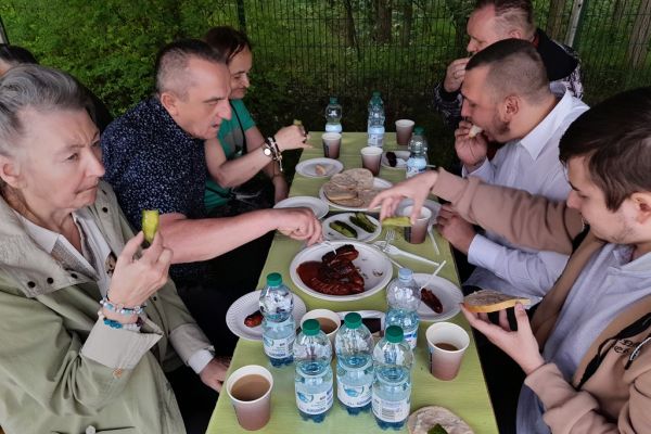 Mieszkańcy przy poczęstunku siedzą i jedzą.