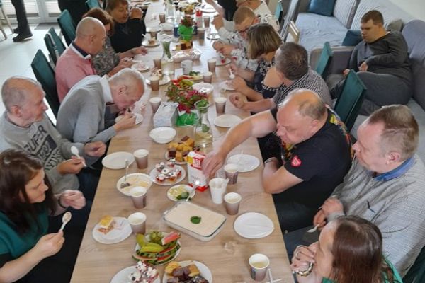 Mieszkańcy wraz z innymi uczestnikami biesiady siedzą  przy długim stole.