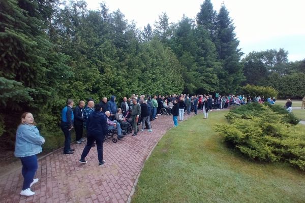 Mieszkańcy podczas szkolenia stoją ustawieni na ścieżkach w terenie wokół domu.