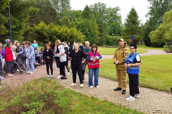 Mieszkańcy podczas szkolenia stoją ustawieni na ścieżkach w terenie wokół domu.