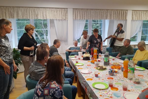 Mieszkańcy siedza przy stole z poczęstunkiem podczas urodzin Mieszkańca.