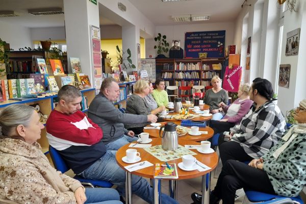 Mieszkańcy siedzą przy stolikach w bibliotece i czytaja wiersze.